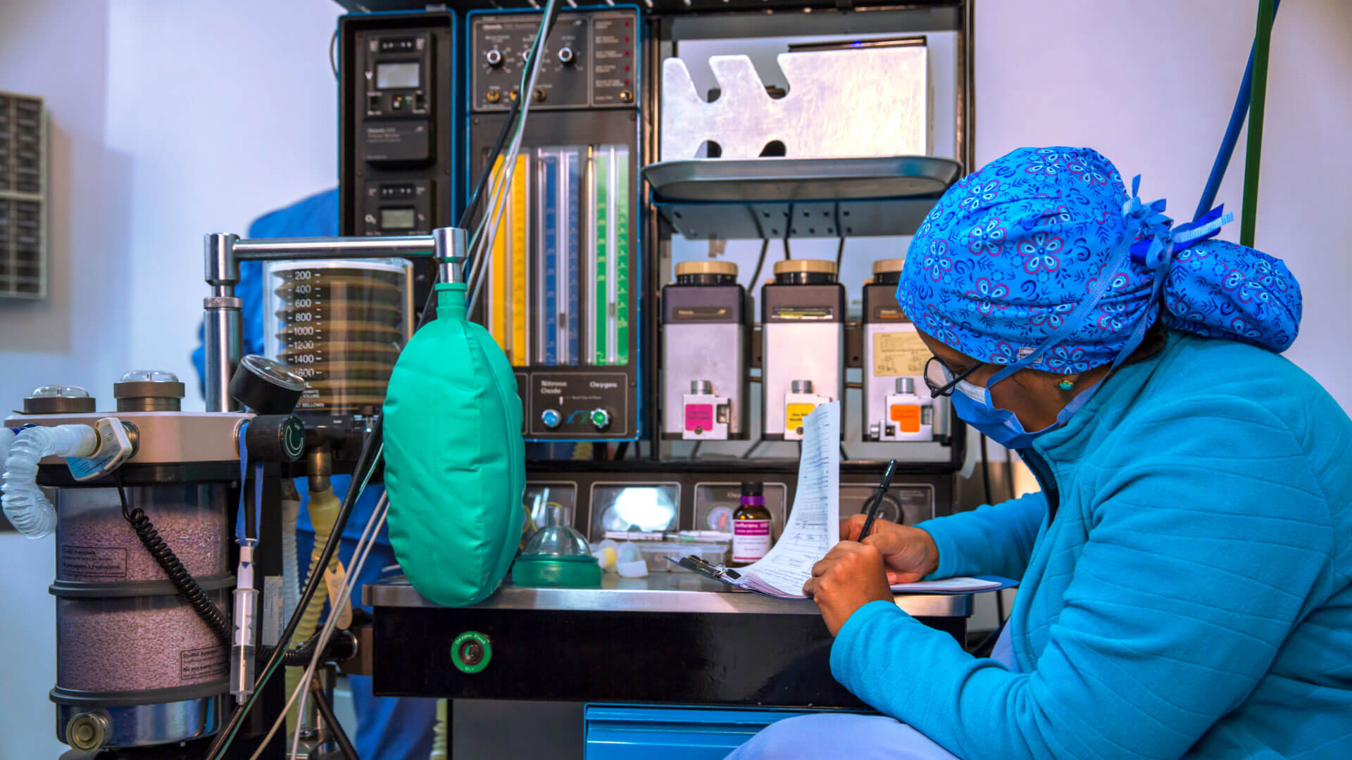 An anesthesiologist who is becoming a CRNA is writing on a piece of paper in front of a machine