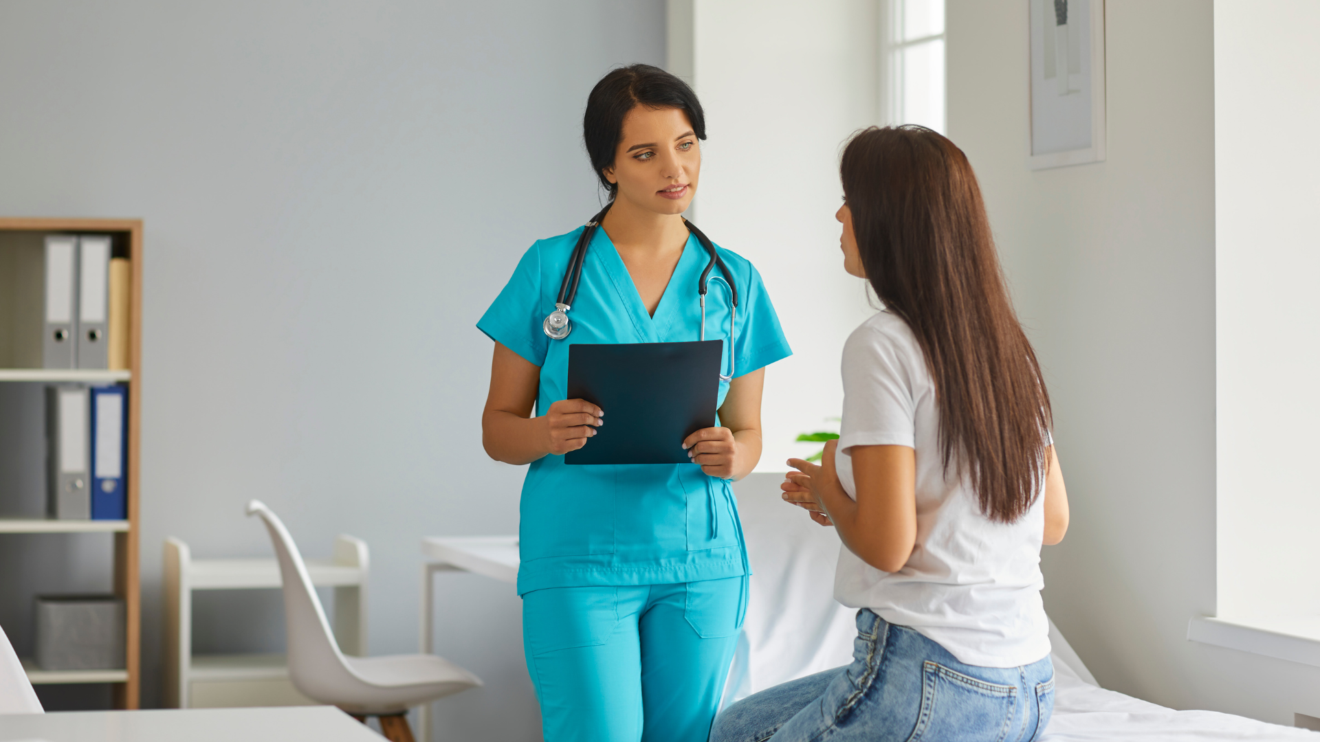 CRNA in blue scrubs reviewing a case with the patient before a procedure in an ambulatory surgery center